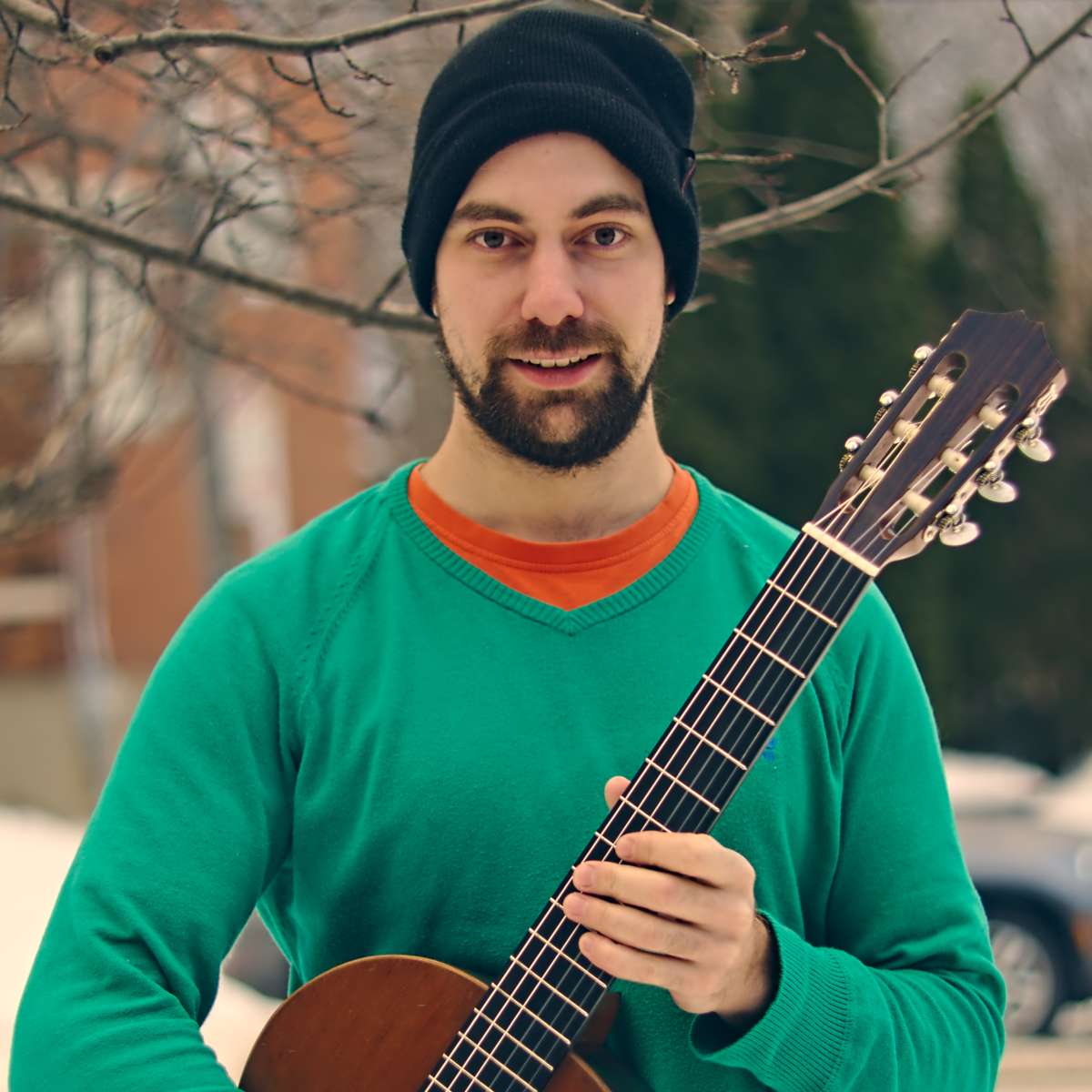 Brett holding a classical guitar wearing a green sweater and black tuque.