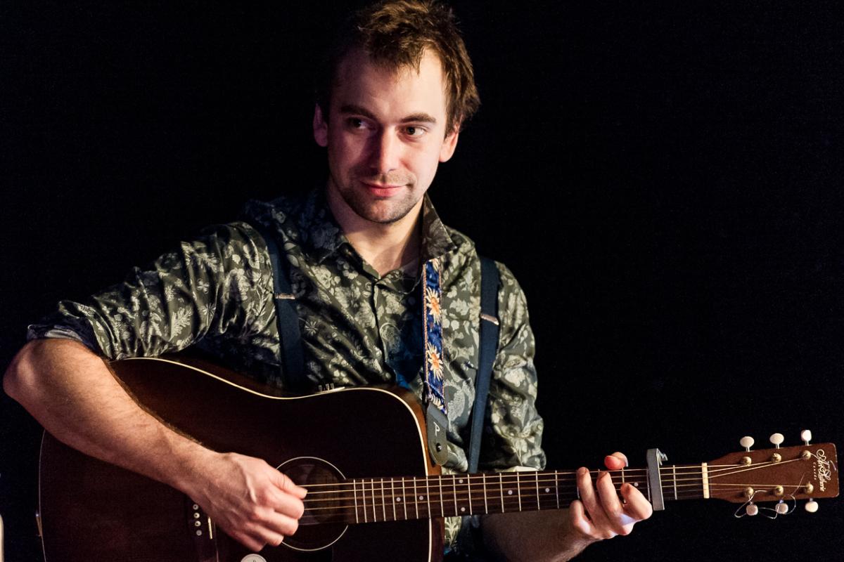 Brett playing fingerstyle guitar and wearing a green shirt at a performance