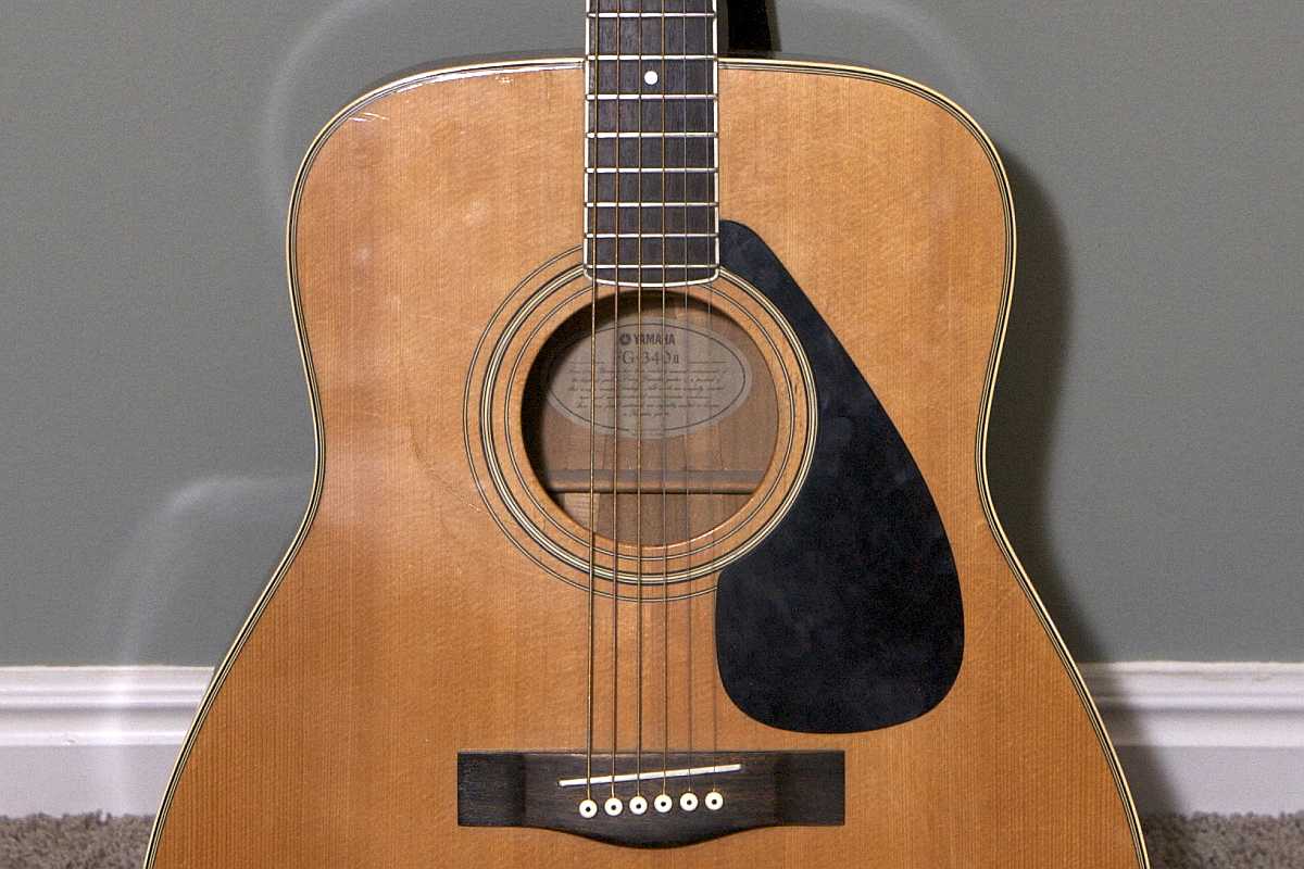 The headstock of a Yamaha acoustic guitar leaning against a grey wall.