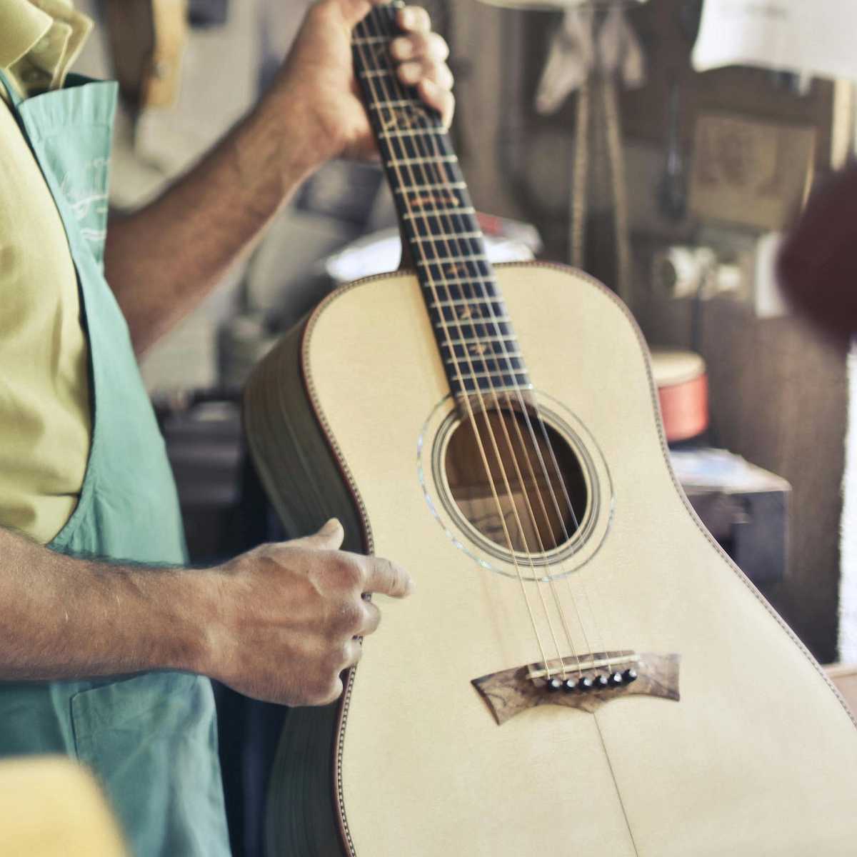 A luthier holding up a recently constructed acoustic guitar made from an excellent tonewood