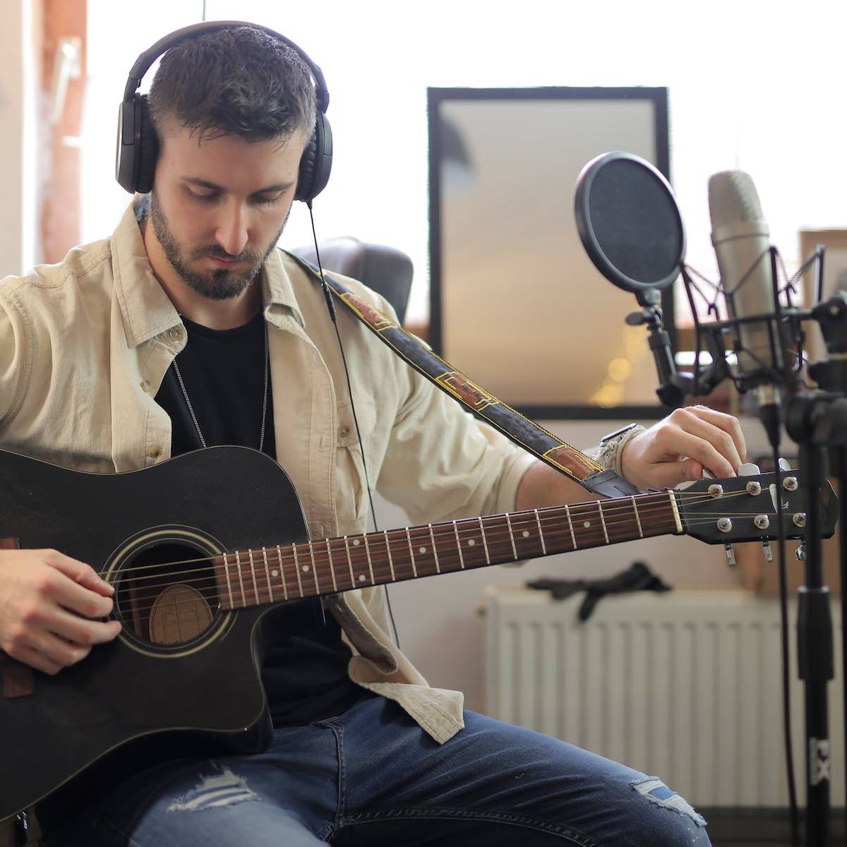 A man tuning the sixth string of a black acoustic guitar to get into an alternate tuning