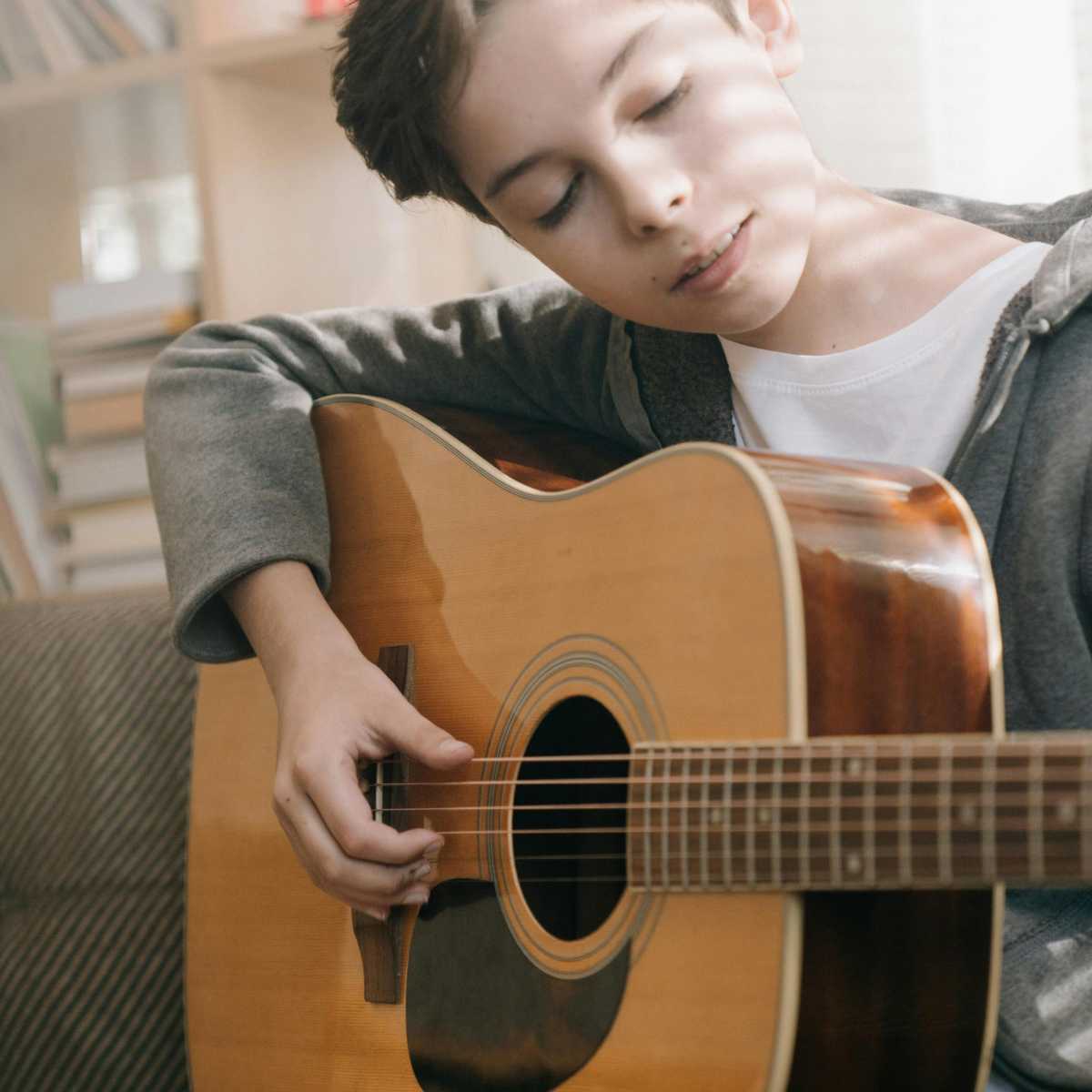 A young boy playing the acoustic guitar fingerstyle while looking at the fretting hand