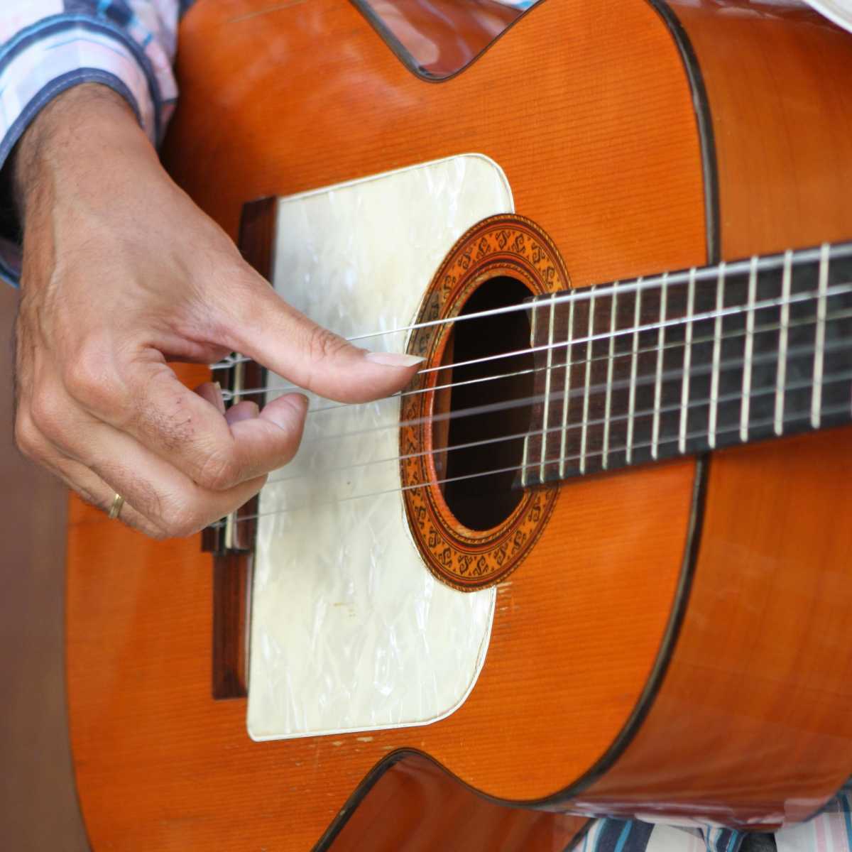 A flamenco guitarist with a white golpeador on his instrument playing the fifth string with his thumb using alzapua