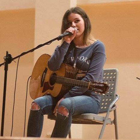 Gabriella Quevedo speaking onstage with a Taylor guitar at an event in Taiwan. 
