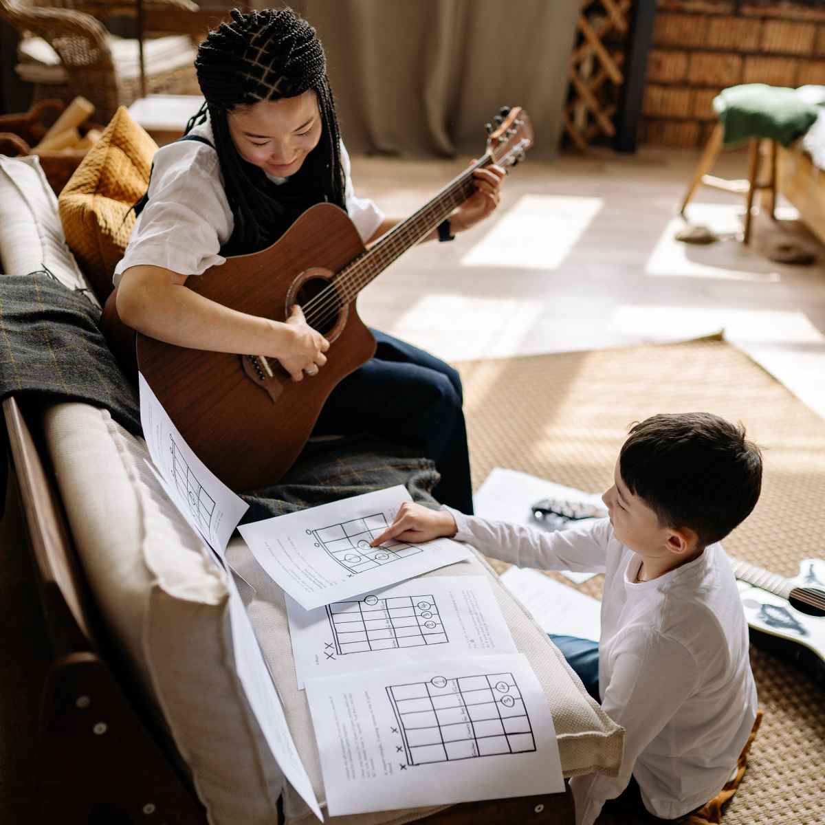 An image of a girl and boy practicing guitar with a chord chart