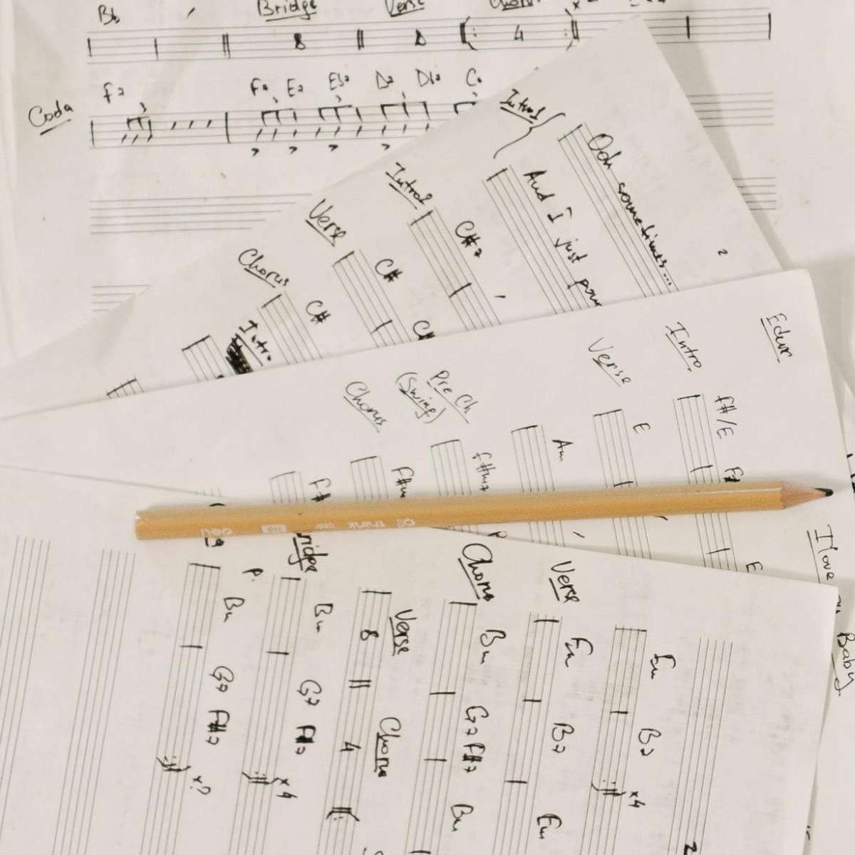 A top-down view of several guitar tablatures written on a piece of paper with a pencil sitting in between them