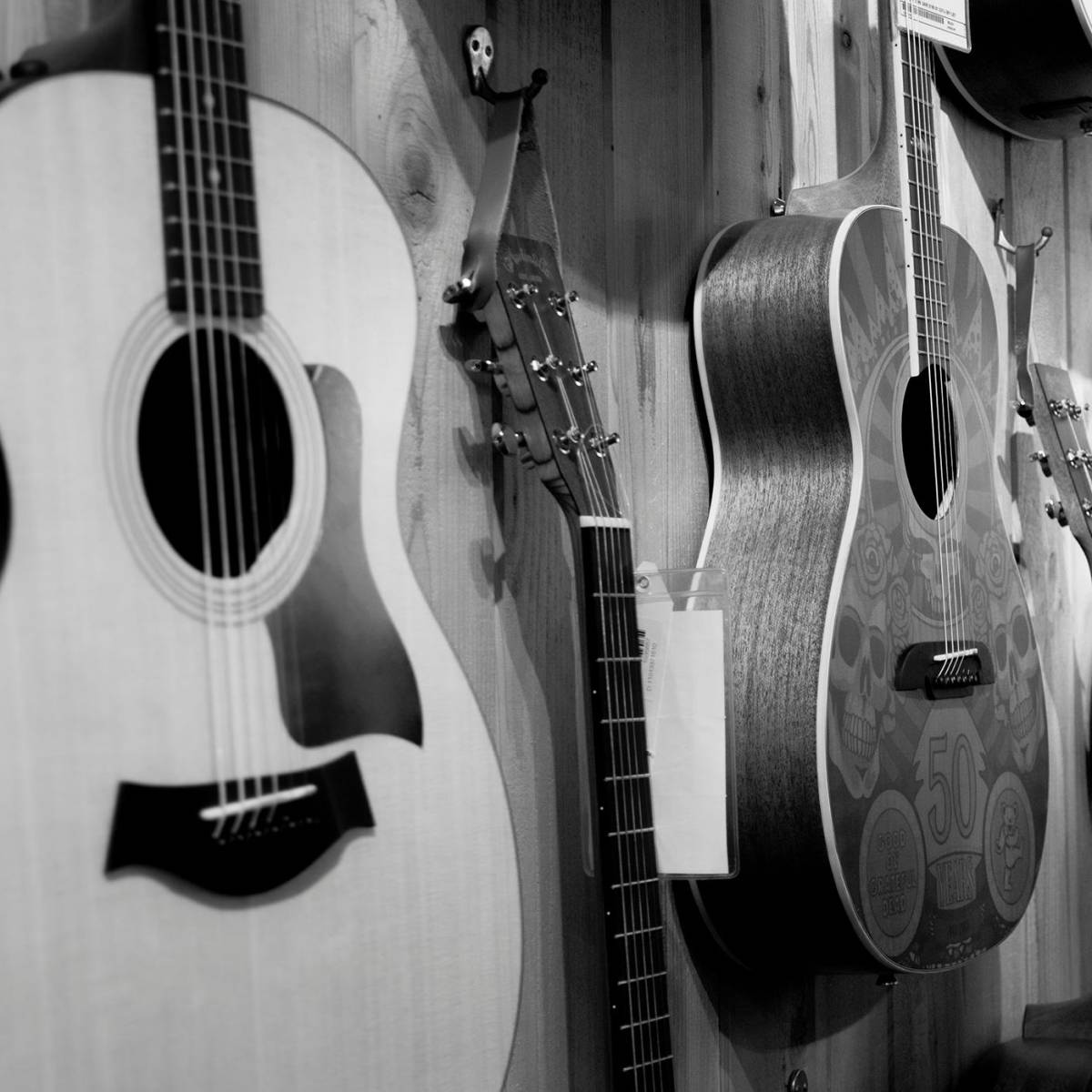 A black-and-white photo of a line-up of steel string guitars hanging on the wall