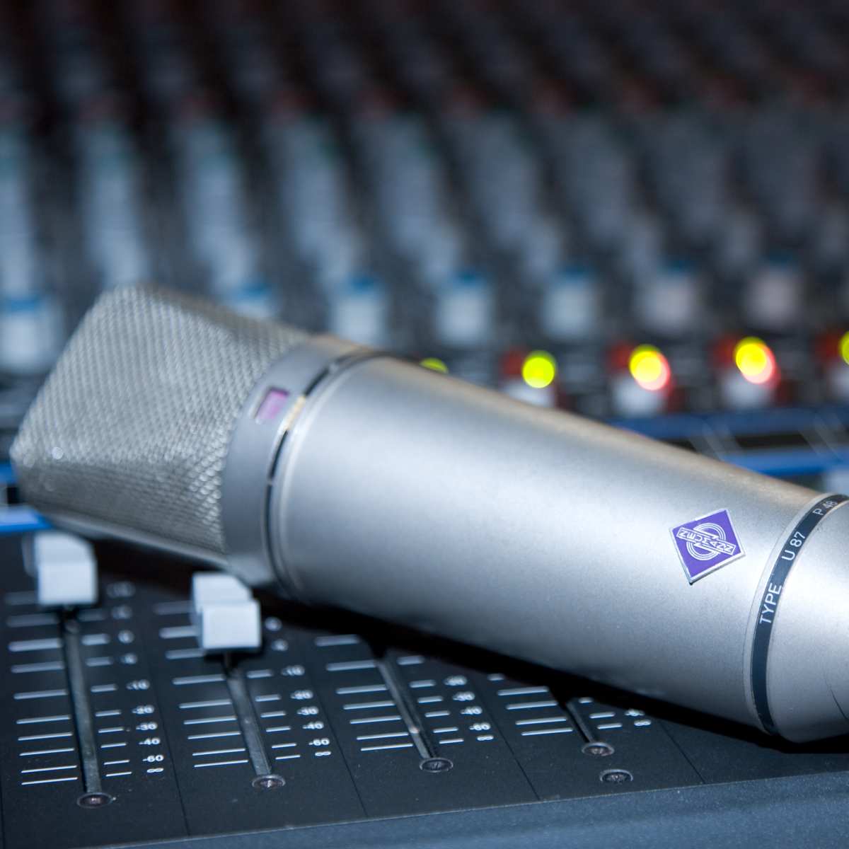 A Neumann U87 microphone resting on a professional audio console.