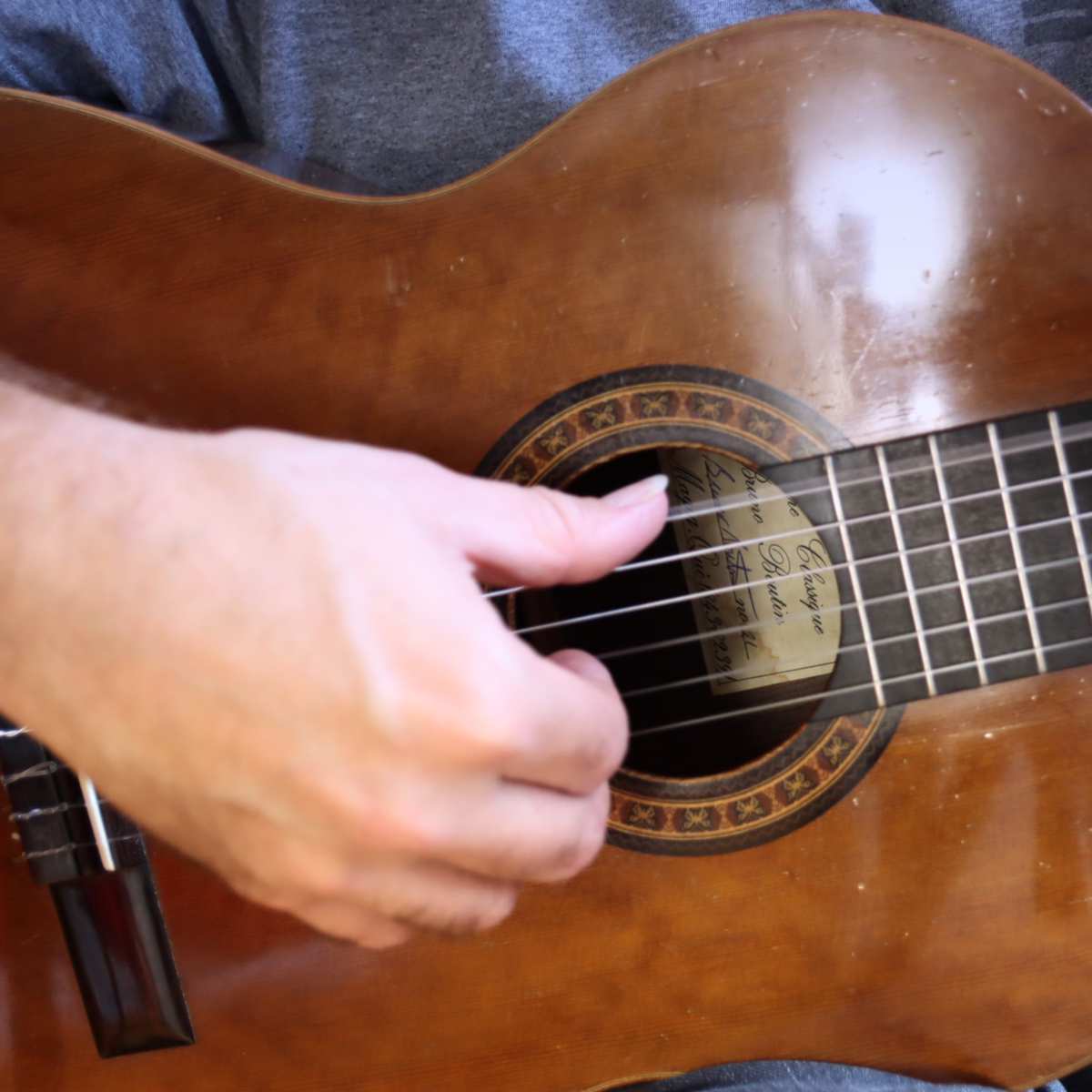 A close up view of the thumb plucking the sixth string of a classical guitar
